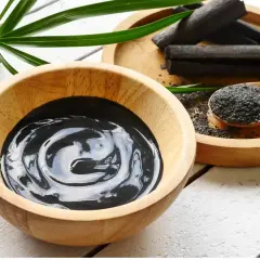 Una ciotola di crema nera, bastoncini e polvere di carbone vegetale, pronti per un trattamento purificante.