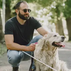 Uomo con glaucoma accarezza il suo cane guida in un parco.