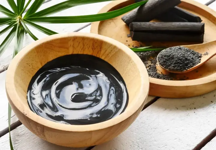 Una ciotola di crema nera, bastoncini e polvere di carbone vegetale, pronti per un trattamento purificante.