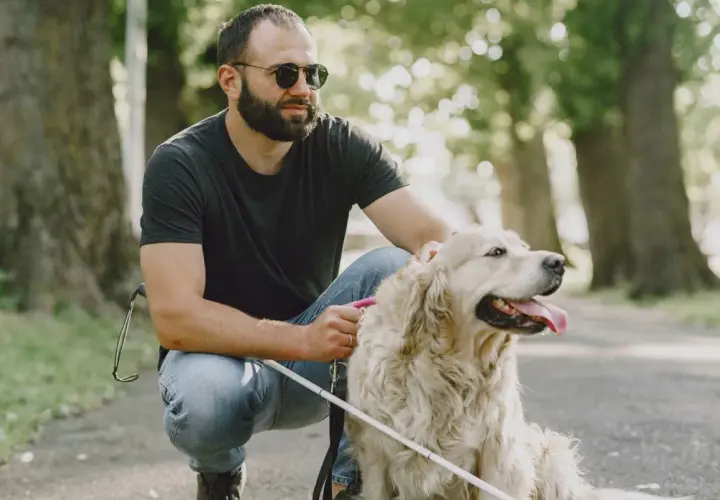 Uomo con glaucoma accarezza il suo cane guida in un parco.