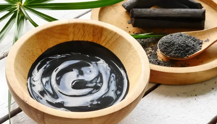 Una ciotola di crema nera, bastoncini e polvere di carbone vegetale, pronti per un trattamento purificante.