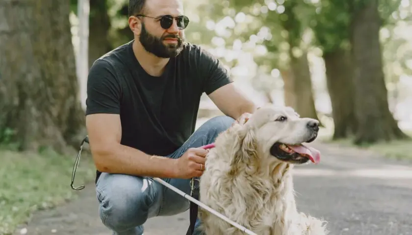 Uomo con glaucoma accarezza il suo cane guida in un parco.