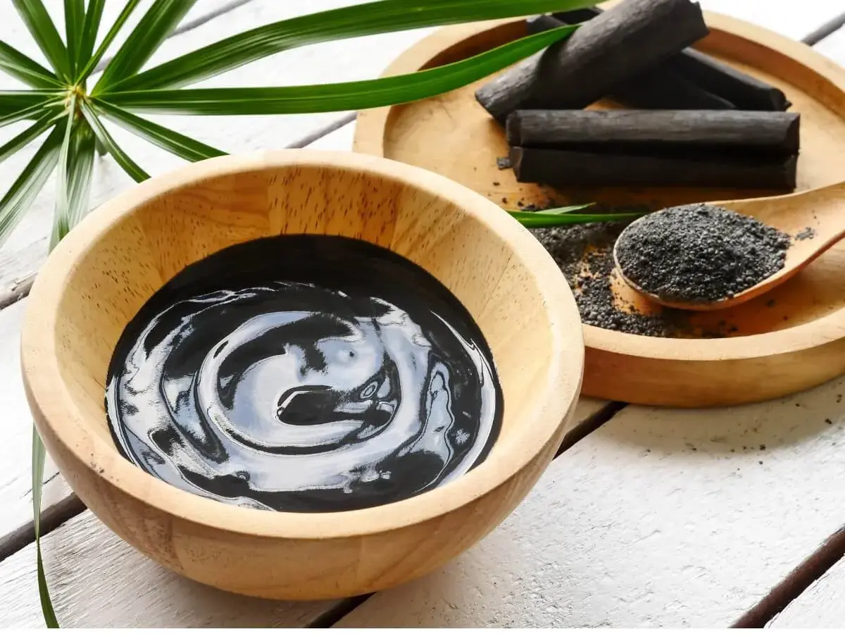 Una ciotola di crema nera, bastoncini e polvere di carbone vegetale, pronti per un trattamento purificante.