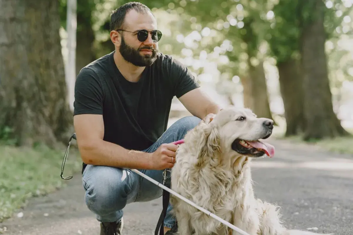 Uomo con glaucoma accarezza il suo cane guida in un parco.